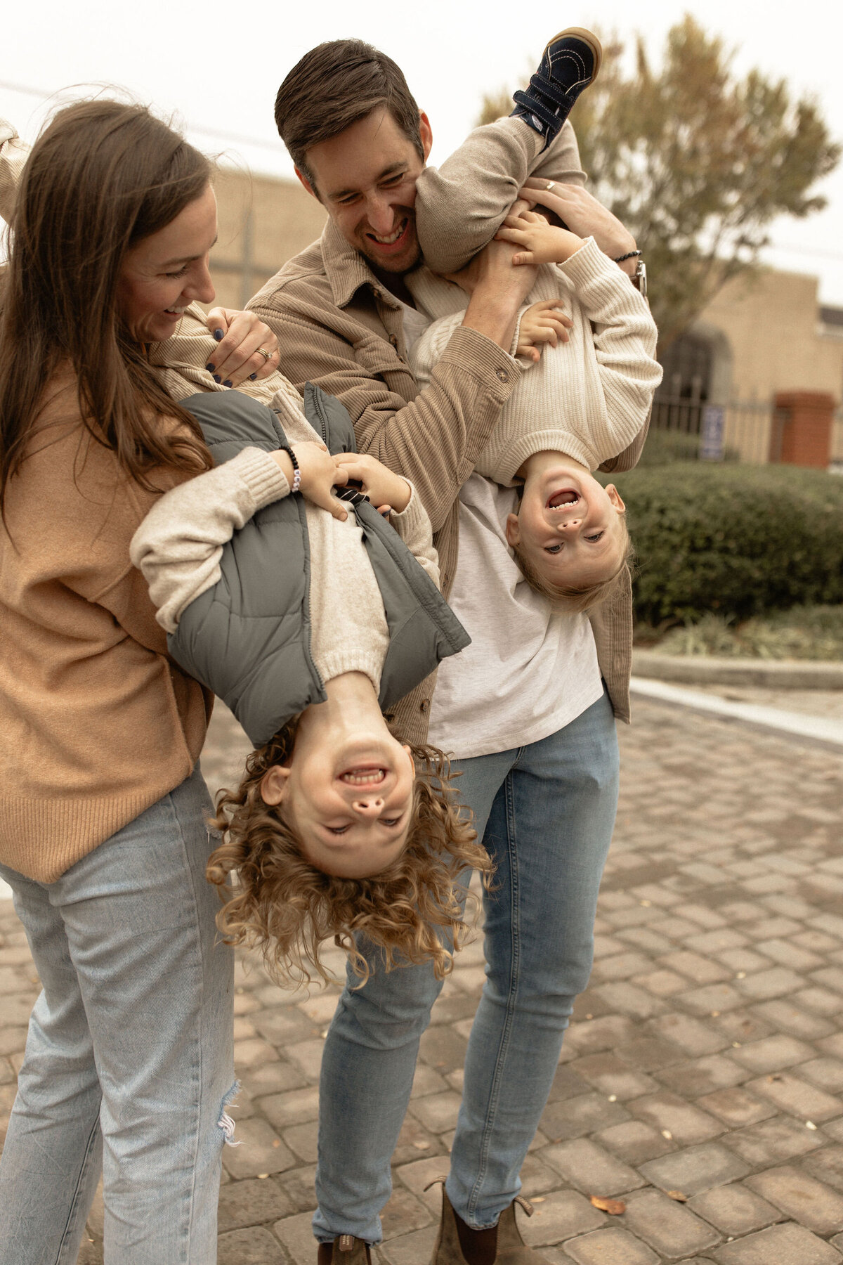 A mom and dad playfully hold their two giggling toddler boys upside down.