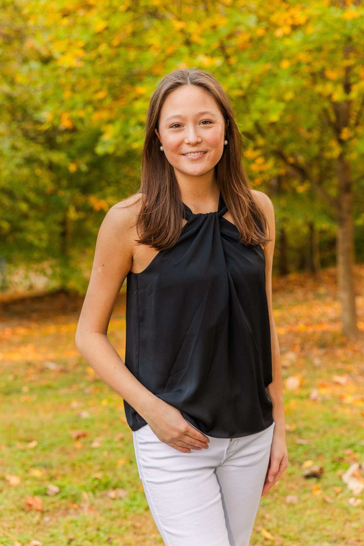 senior girl wearing white jeans and black top ankles crossed hand in pocket during photo session in a Buckhead park