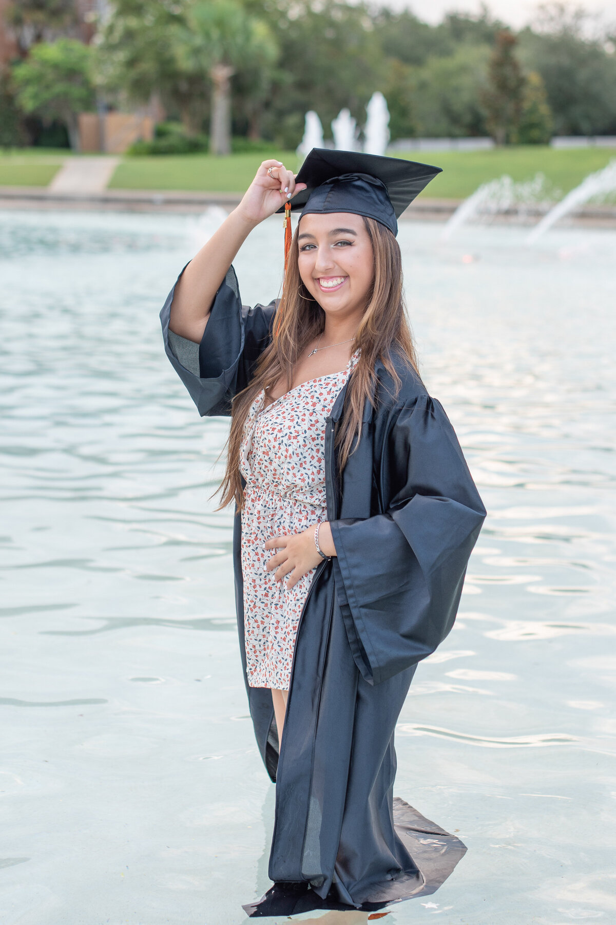 High school senior girl in cap and gown poses in a pond.