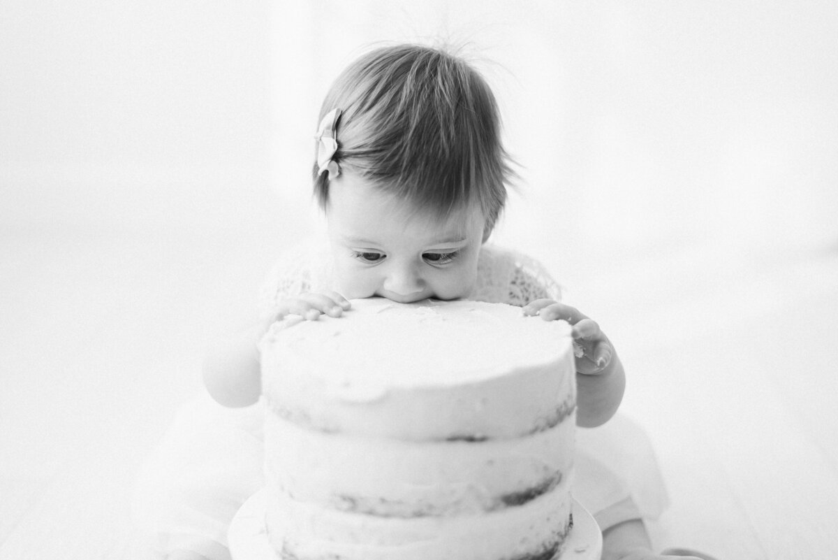 One year old girl eating birthday cake without hands during cake smash photoshoot west sussex