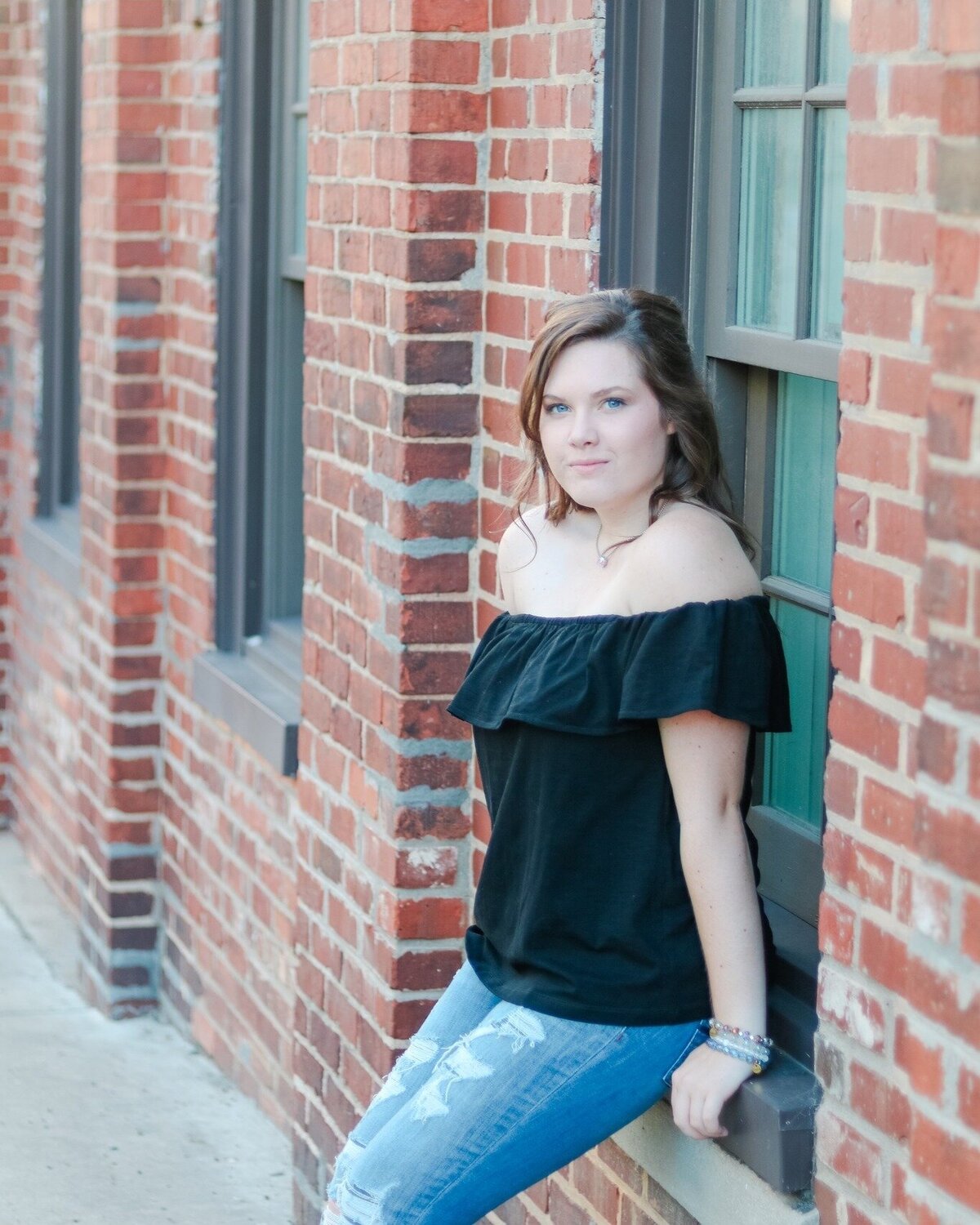 Senior girl sitting in window of a brick building