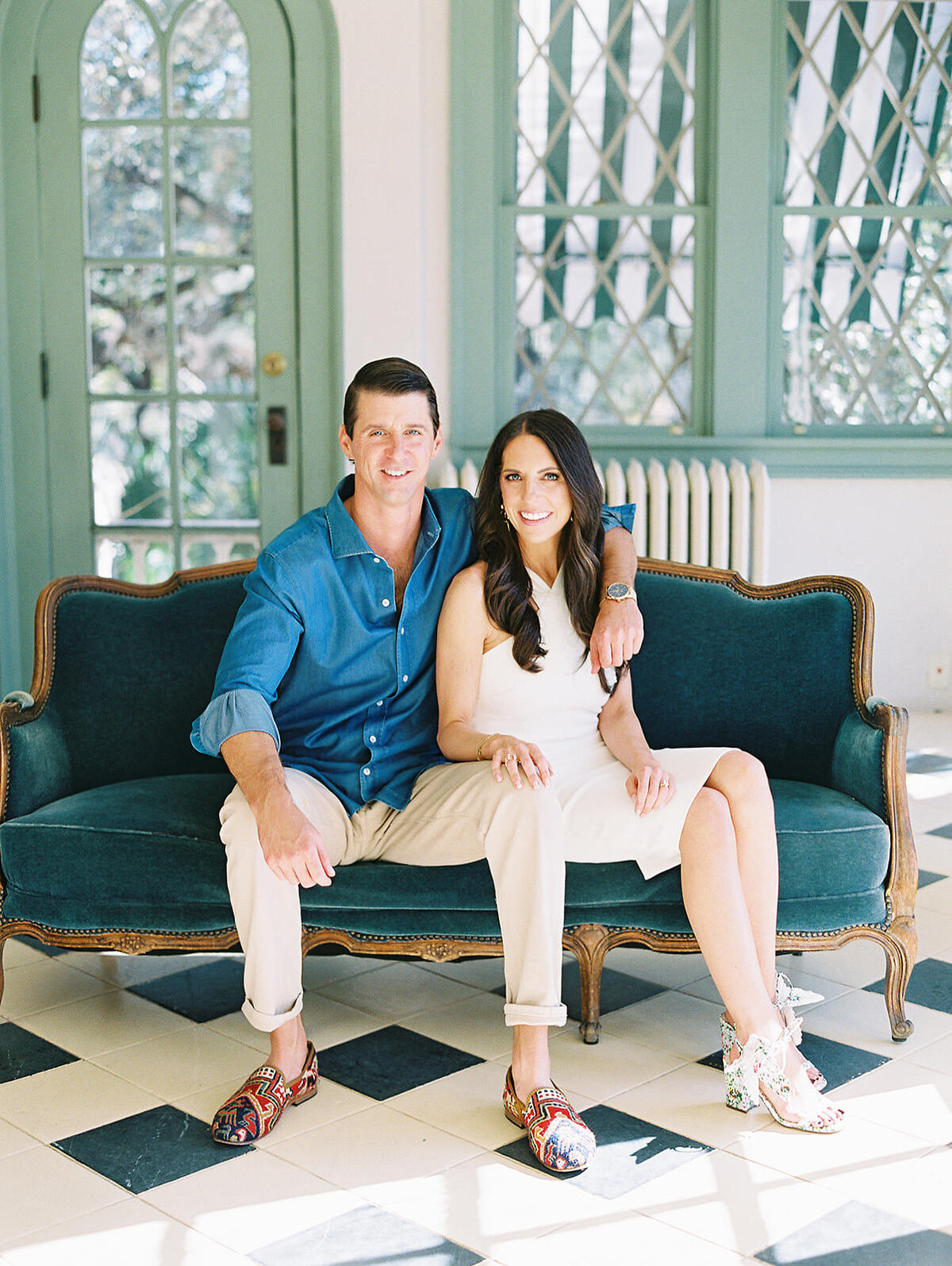 A classic modern couple pose together on a blue velvet couch in the sunroom at Laguna Gloria
