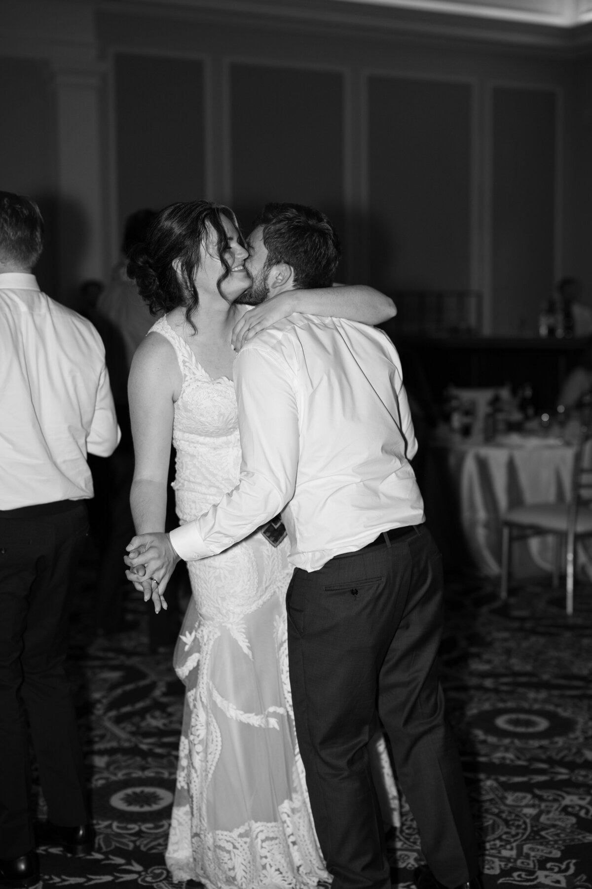 A couple with their arms wrapped around each other smiling as they dance at their reception