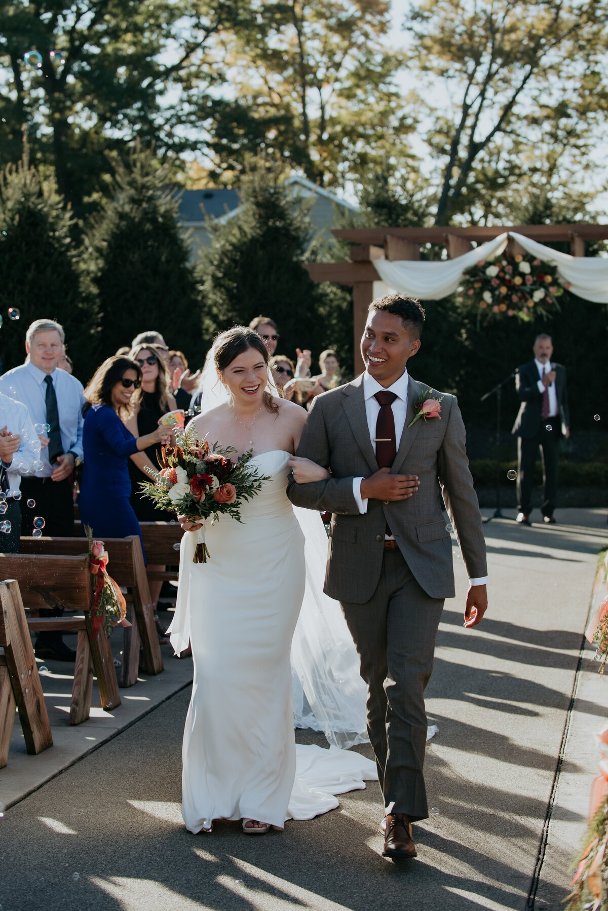 The bride and groom walk with linked arms down the aisle after their first kiss to their guests blowing bubbles.