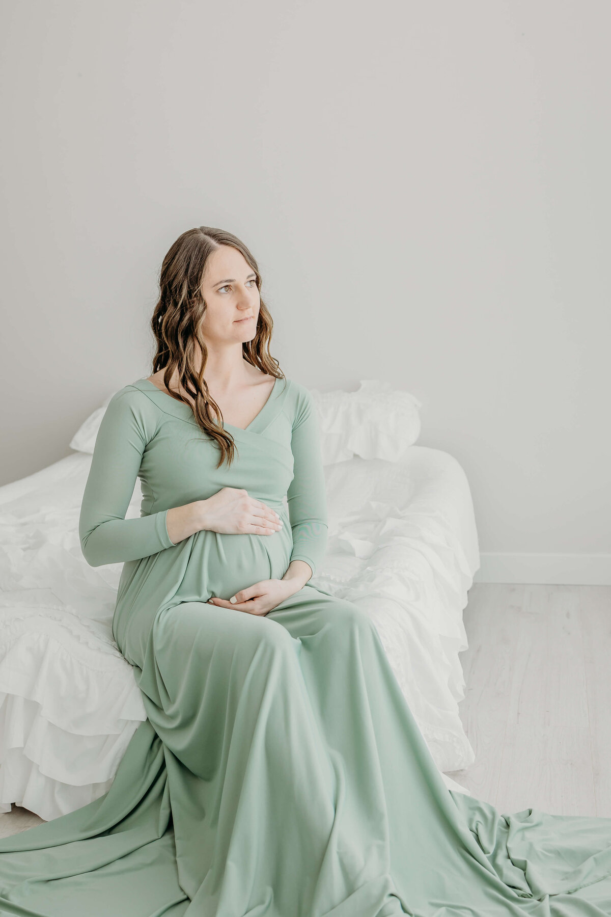 Mother holding belly while sitting on bed in photography studio