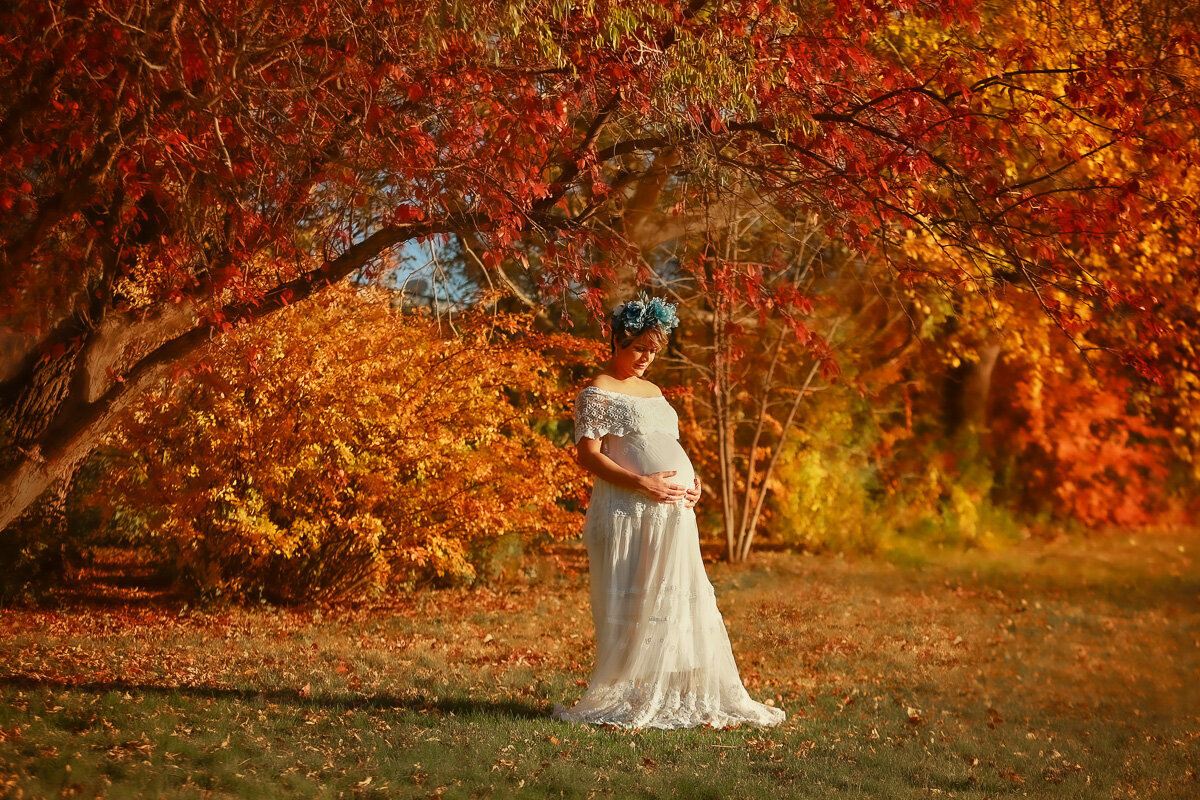 Pregnant mama wearing a white long dress in fall pregnancy photo session in Confederation Park by Calgary Family Photographer.