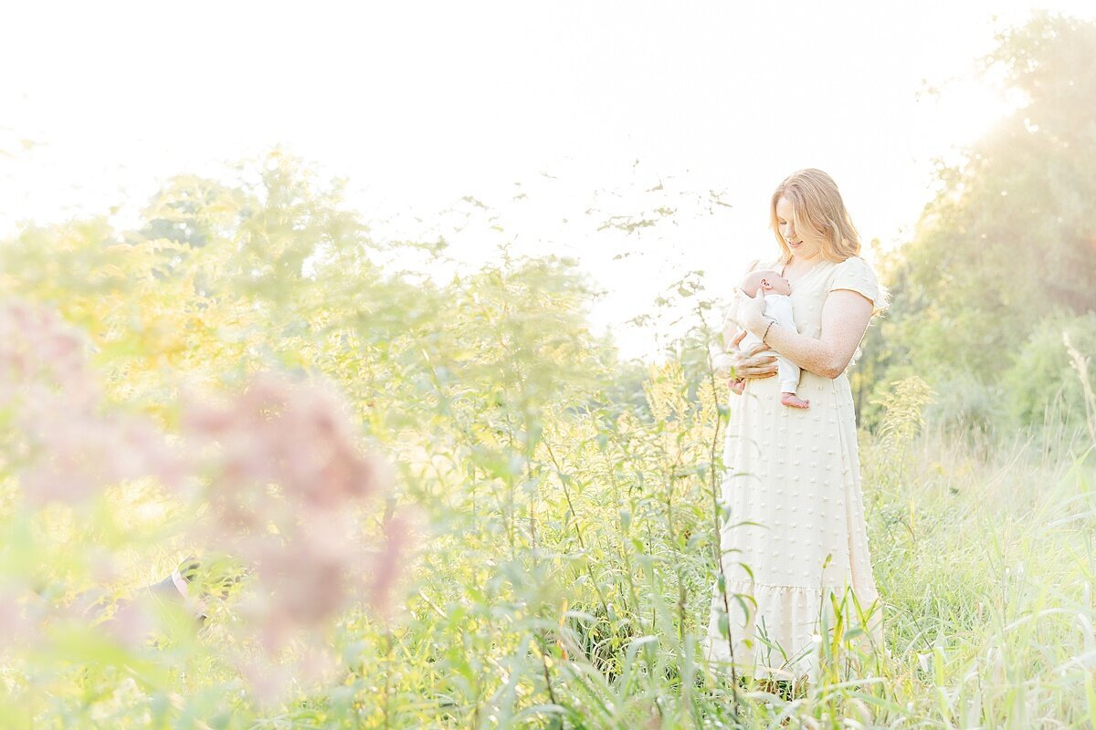mom holds baby in flower field during outdoor newborn photo session at Heard Farm in Wayland Massachusetts with Sara Sniderman Photography