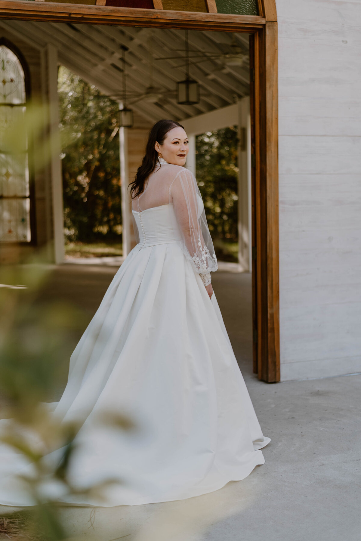 a bride in her wedding dress looking over her shoulder smiling softly. 