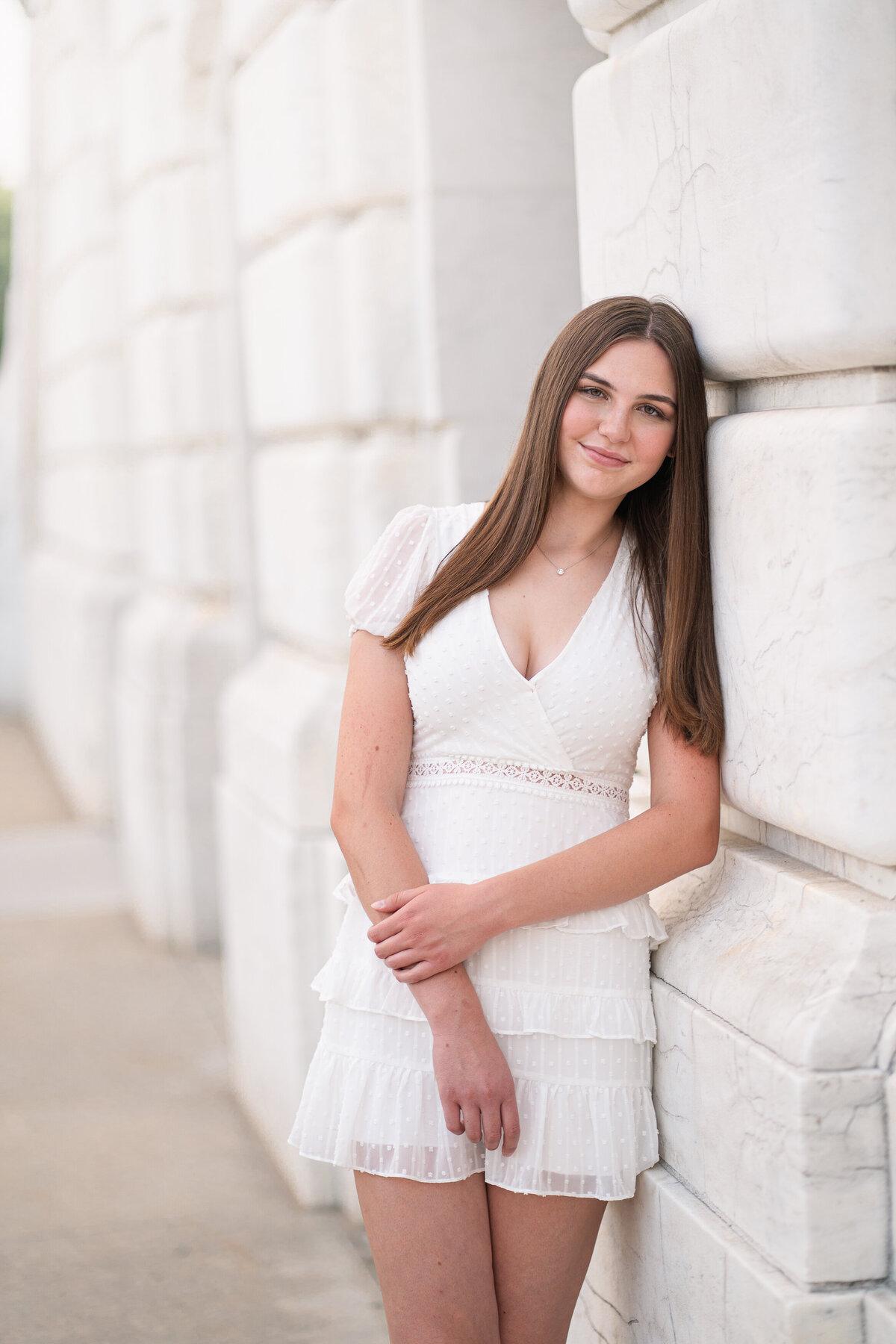 Teenage girl in white dress leaning against white building hold her arm outside of the Detroit Institute of Arts building
