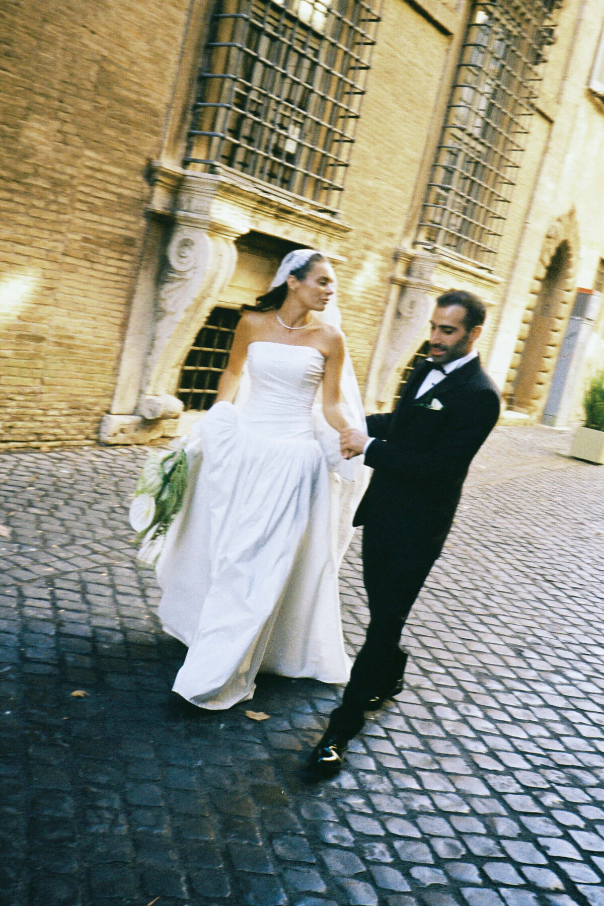 Groom gently adjusting bride’s veil on cobblestone street

