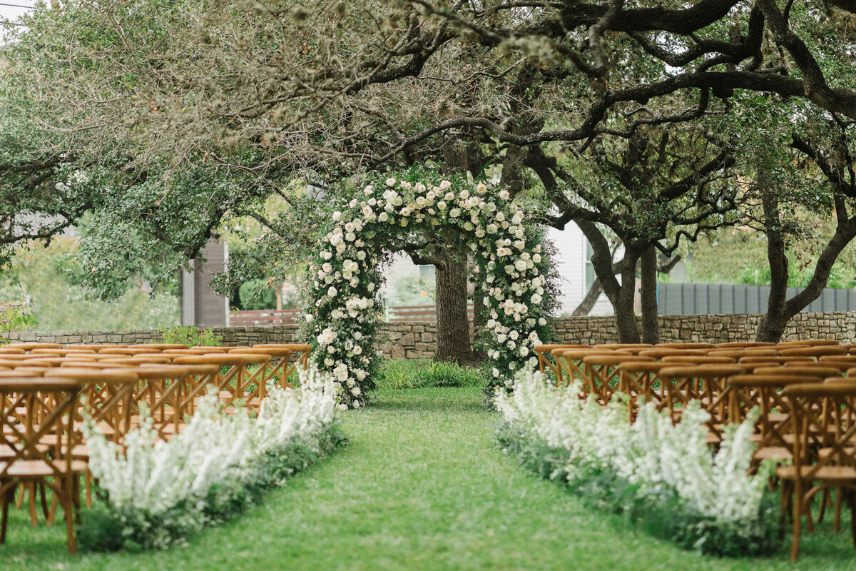 Wedding ceremony design altar Mattie's Austin Venue trees white flower arch brown chairs