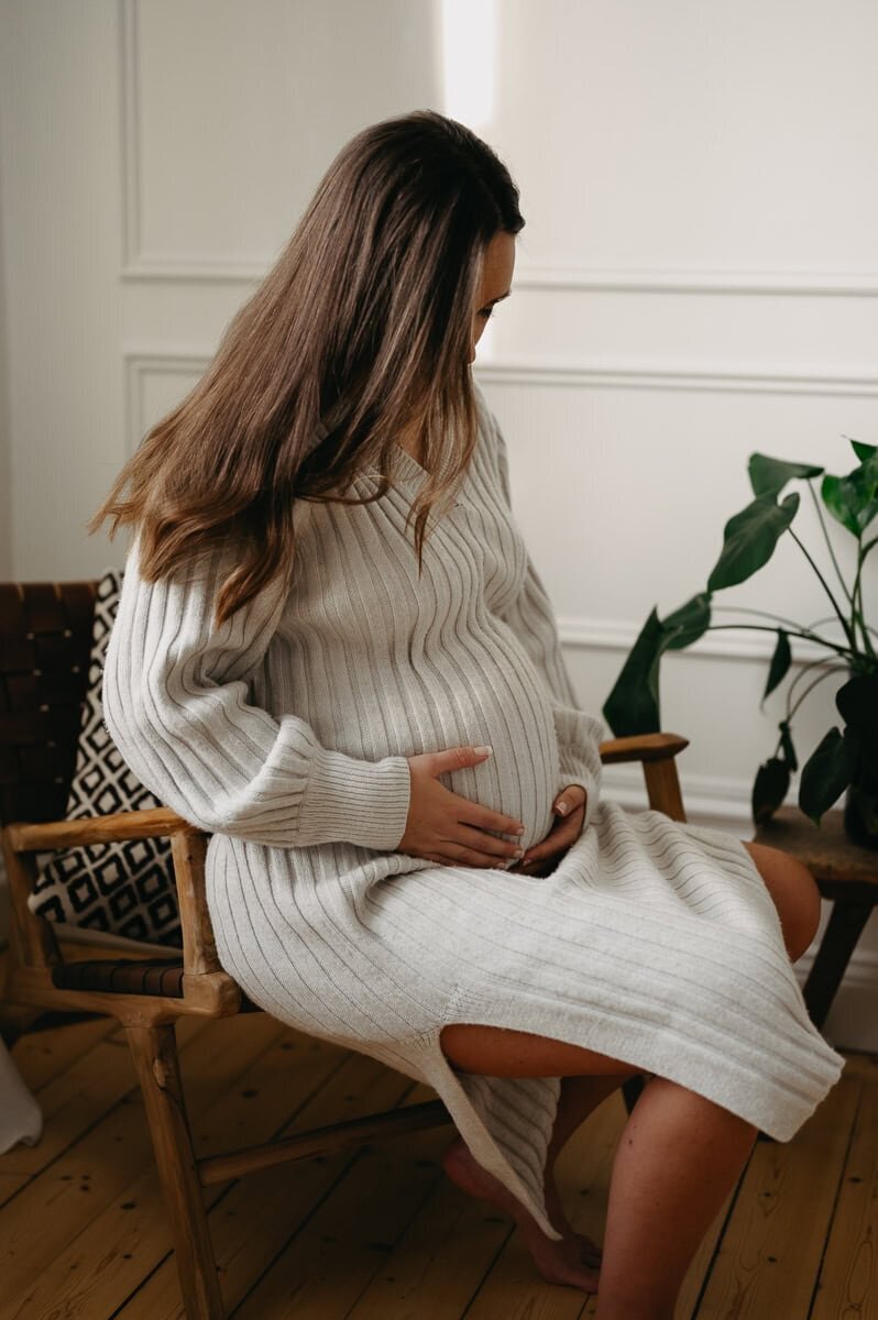 Gravid kvinna sitter i stol och håller om sin mage.