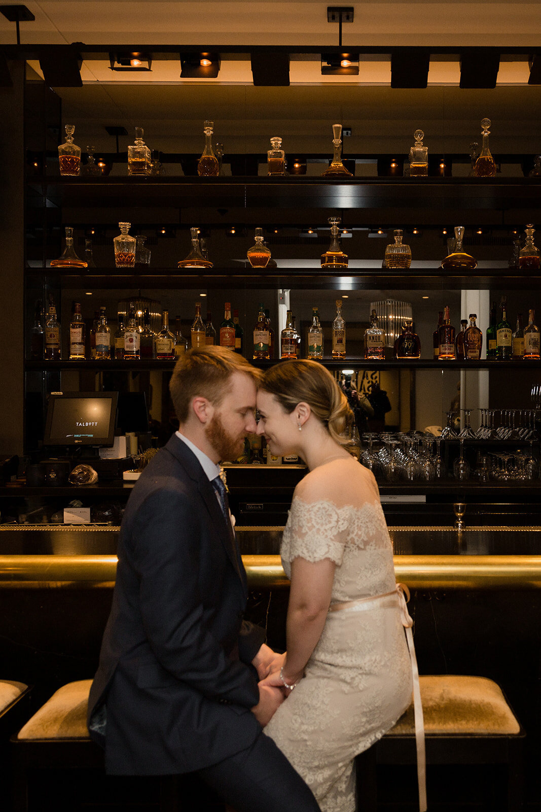 Just Married photo session couple sits on barstools facing each other at a city bar, their foreheads touching