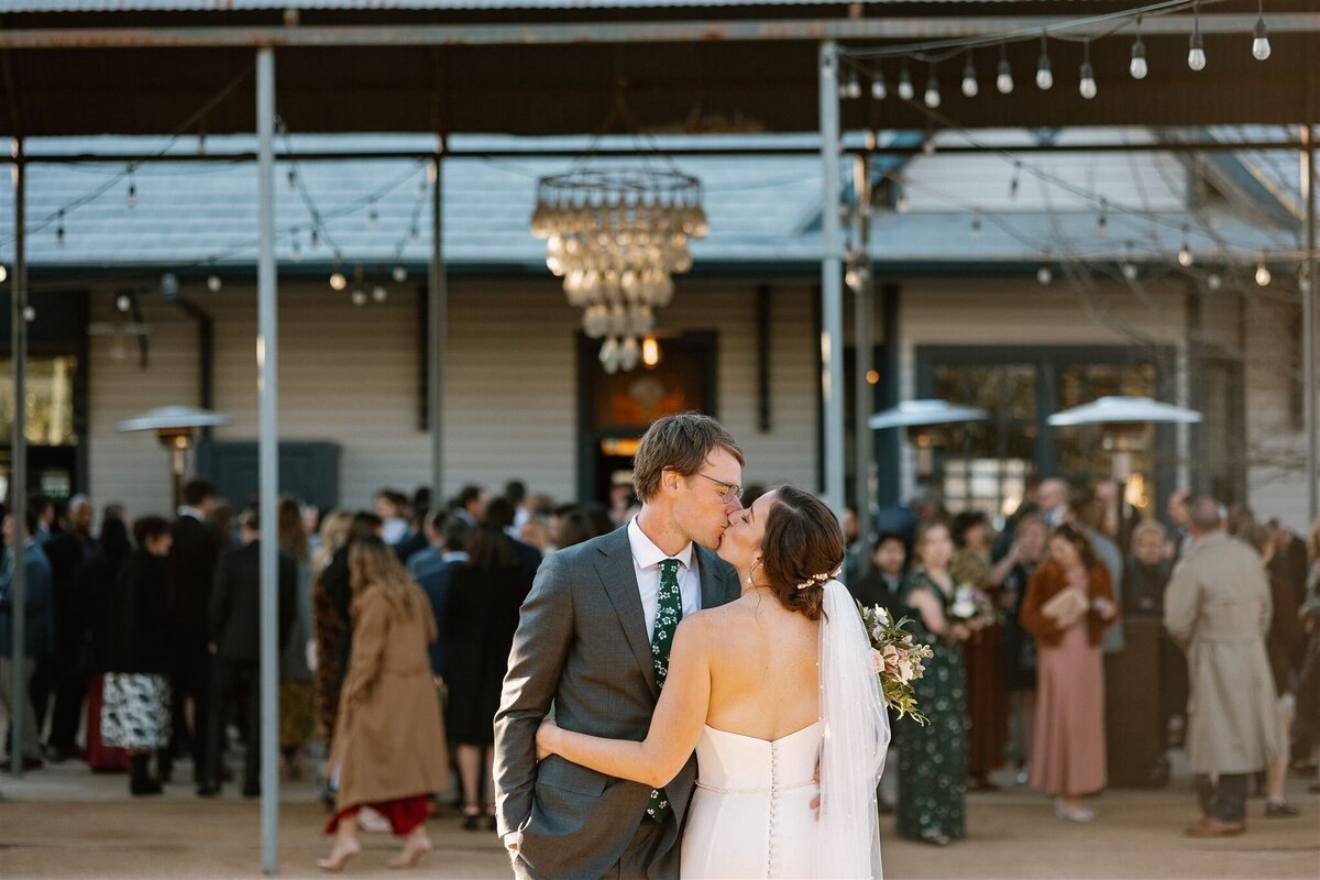 wedding couple kissing with party in the background