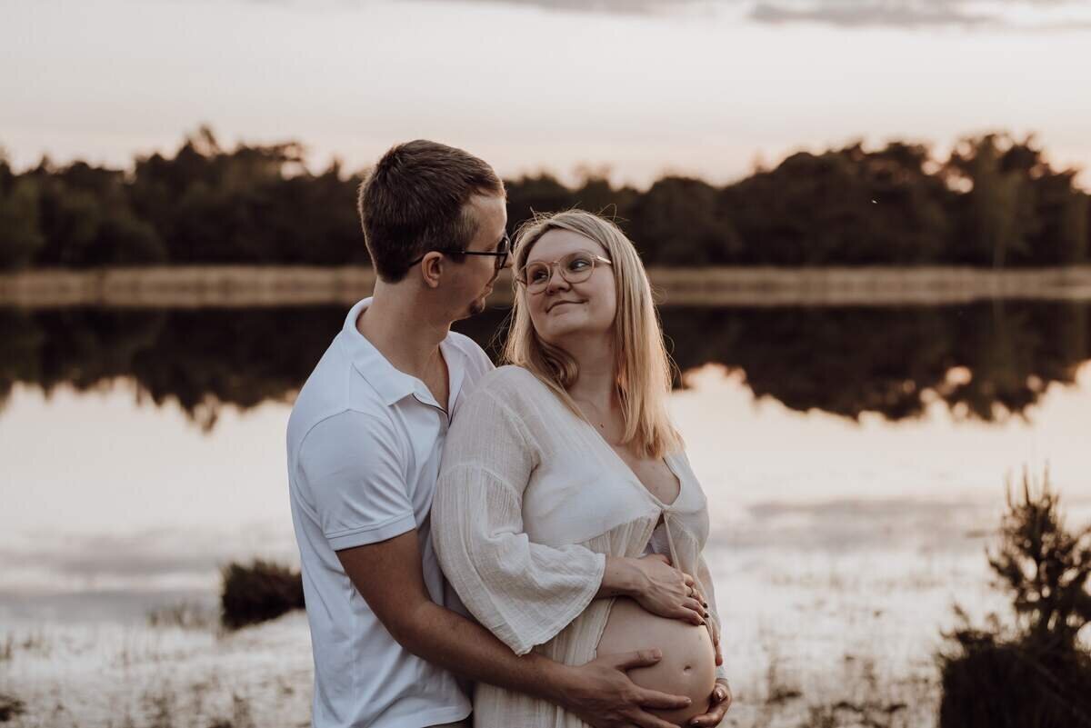 Zwangerschapsfoto van een koppel buiten bij zonsondergang, warme natuuromgeving en intieme momenten tijdens de zwangershoot.