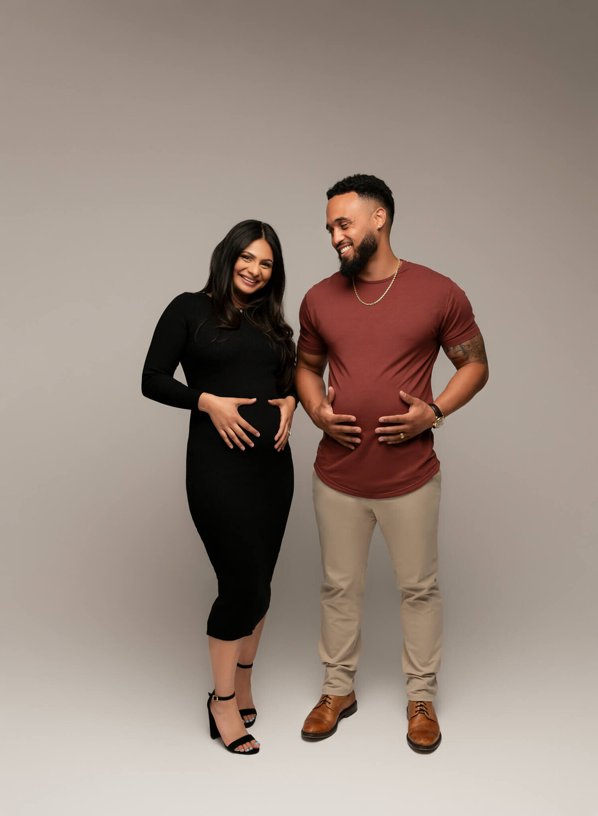 A couple laughing and holding their bellies for a pregnancy announcement photoshoot in austin.