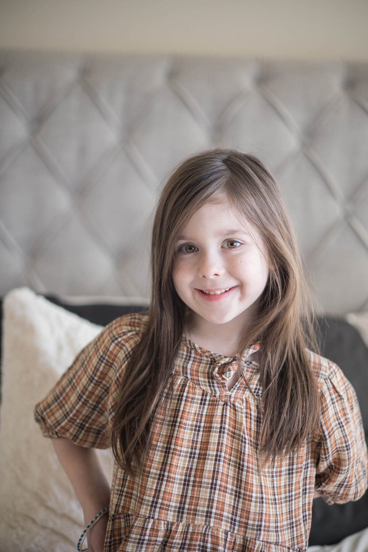 young dark brown haired girl smiling on a gray bed