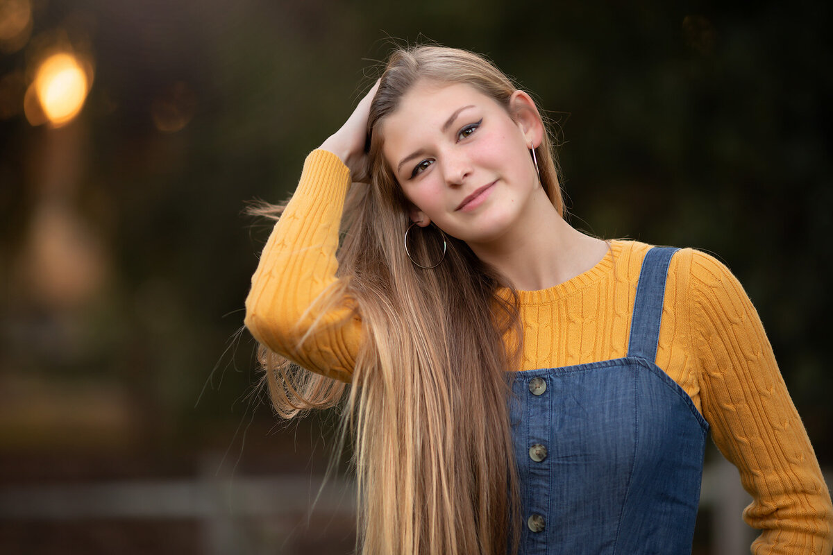 A teenage girl in a yellow sweater and denim dress poses for a Dallas family portrait session, showcasing her joyful expression captured by a Dallas photographer.