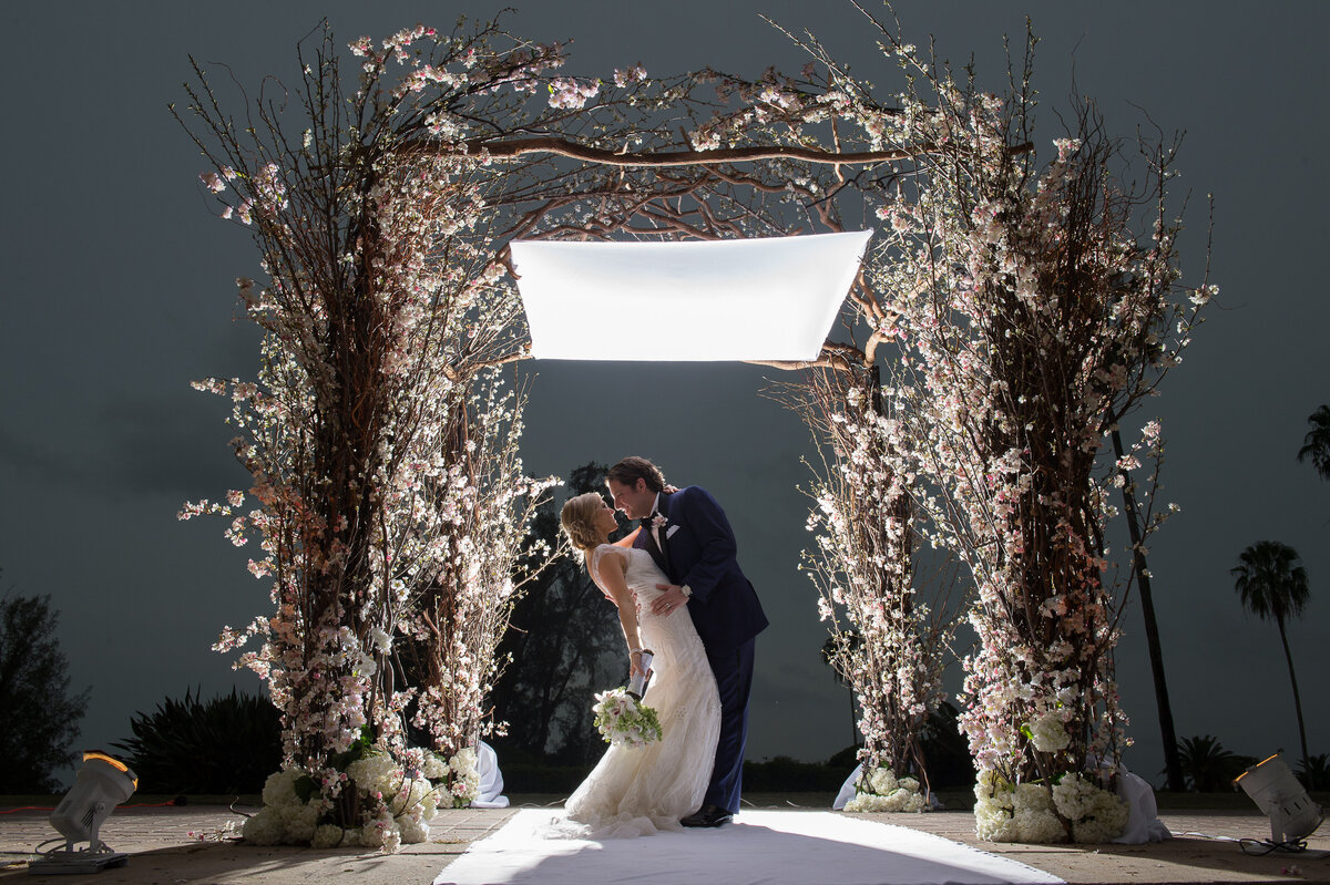 Bride and groom share a romantic moment under a floral arch at night in Miami.