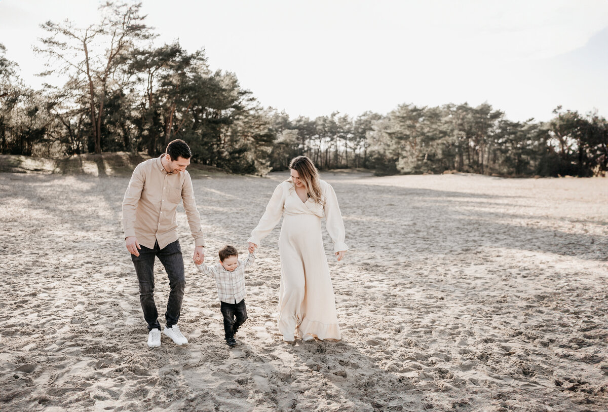 Gezin loopt hand in hand door de Soesterduinen tijdens zwangerschapsshoot.
