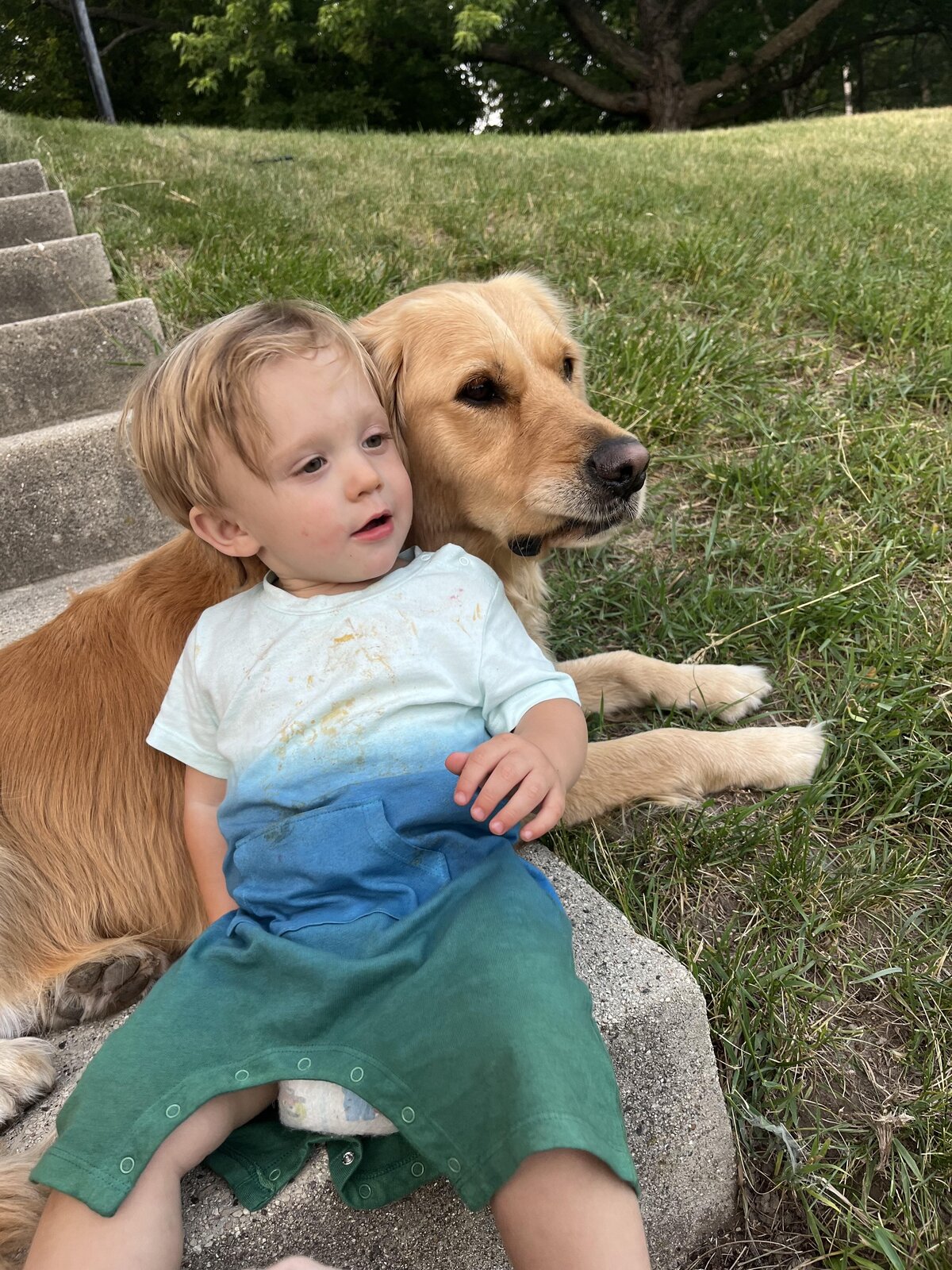 toddler and golden retriever cuddle on steps outside