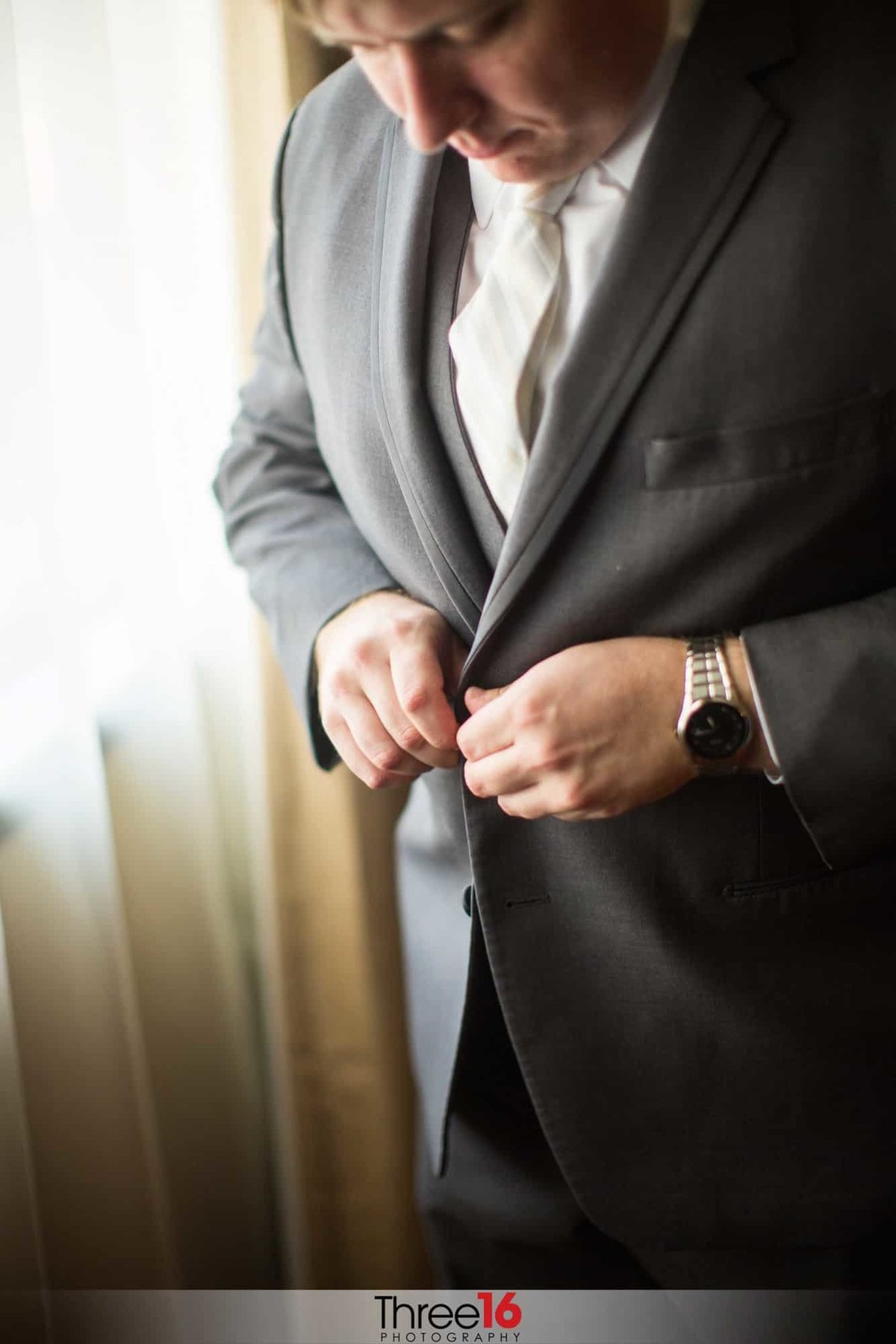Groom buttoning his suit jacket prior to his wedding