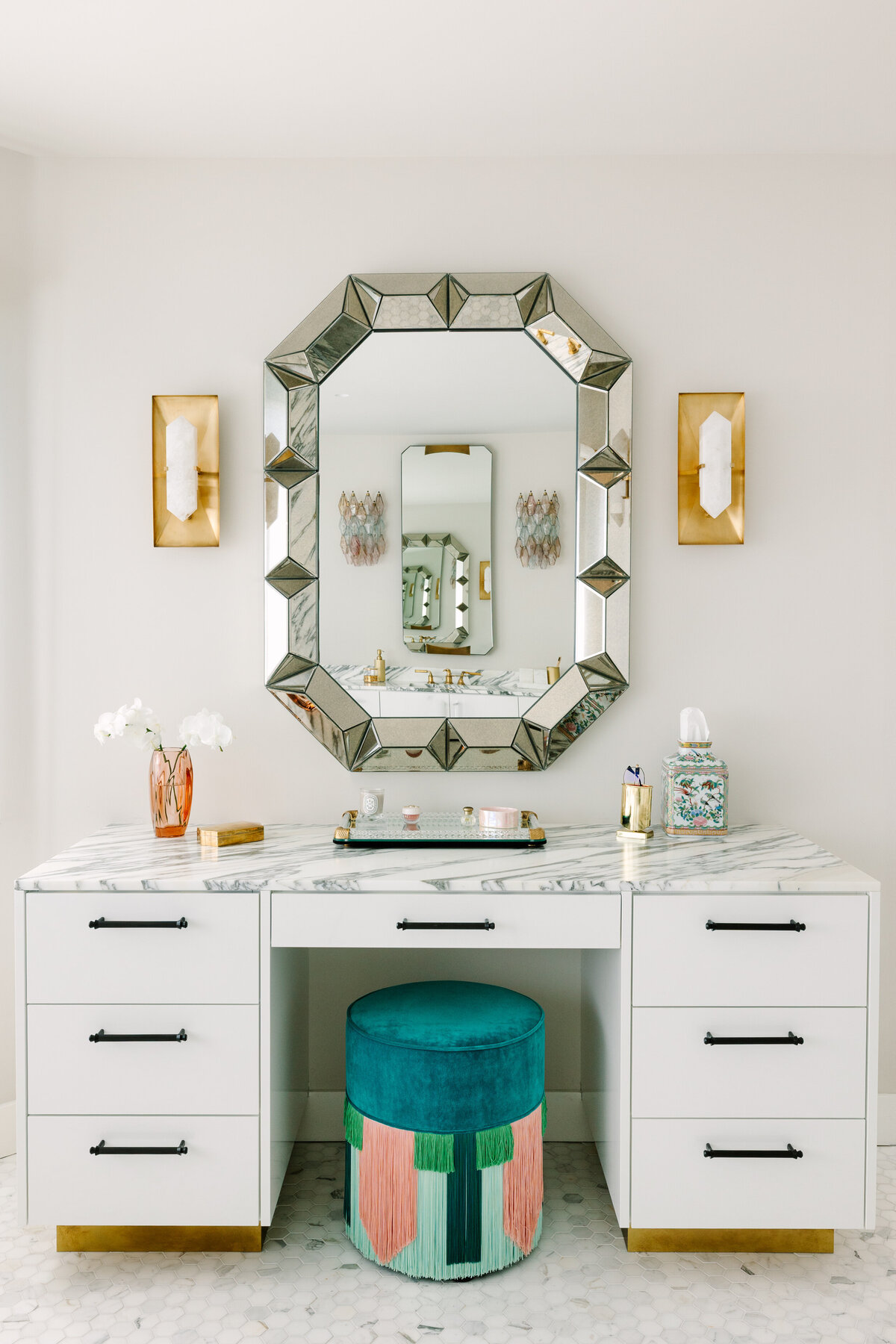 Primary bathroom makeup vanity with white high gloss cabinets and brass base, Arabescato Corchia marble counters, Halcyon Rectangle Sconces by Kelly Wearstler, and Lorenza Bozzoli Couture Emerald Couture Geometric Tie Pouf.