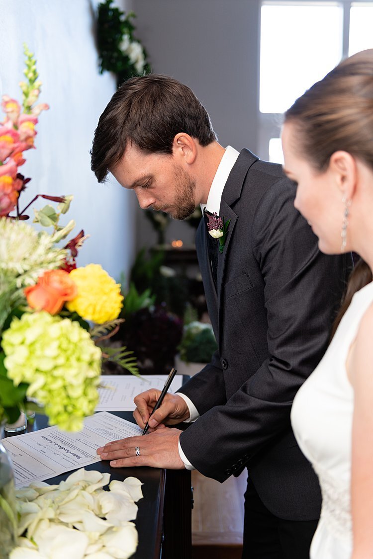 Groom signing marriage certificate as Bride looks on during self-uniting Quaker wedding ceremony in Pittsburgh, PA