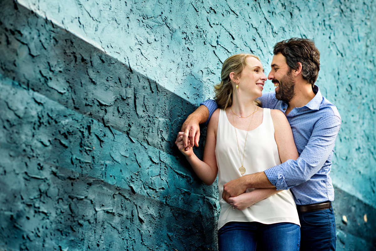 A man holds his fiance while they lean in front of a blue wall on south street.