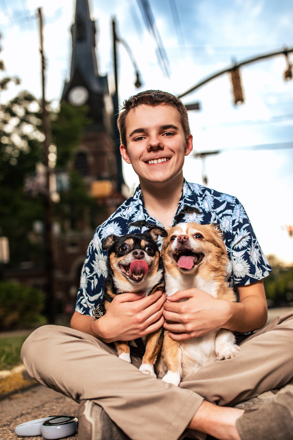 A boy senior brings both dogs to a senior photography session in Sewickley Pennsylvania and poses with them near the clock tower