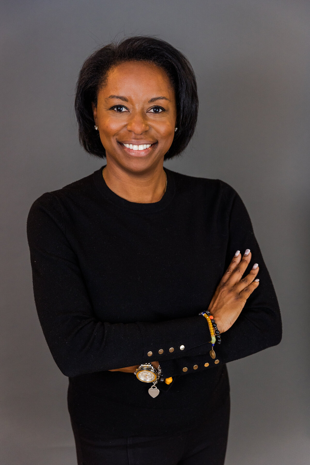 woman wearing a dark dress arms crossed in front of dark gray backdrop in studio during portrait session