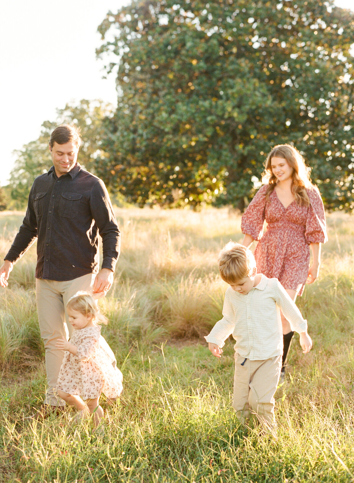Family walks through a field and smiles during a family session at the art museum in raleigh. Image by Raleigh maternity photographer A.J. Dunlap Photography.