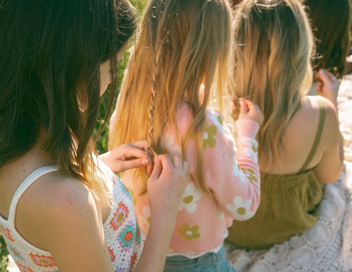 girls braiding mom's hair in outdoor field at summer