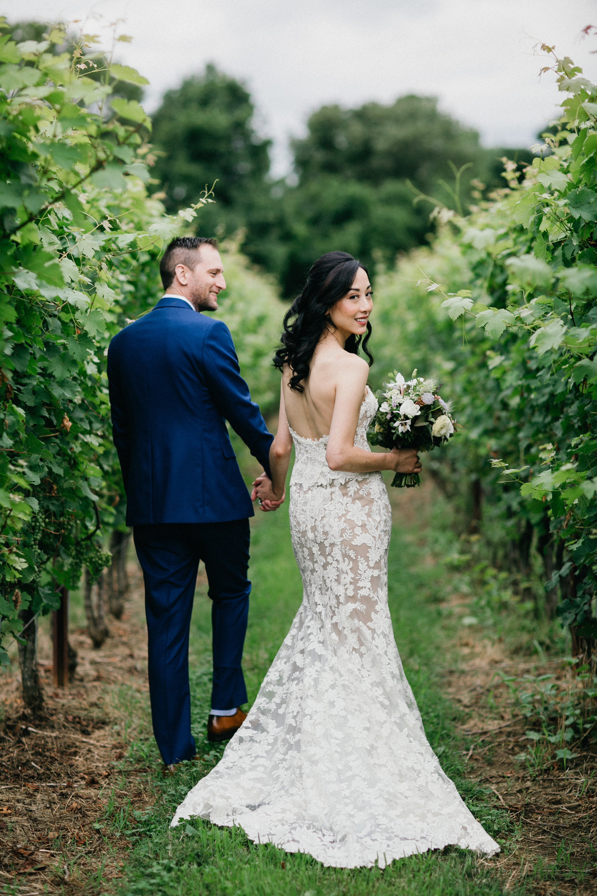 Bride and groom photographed strolling through the rows of grapes at Grace Winery.