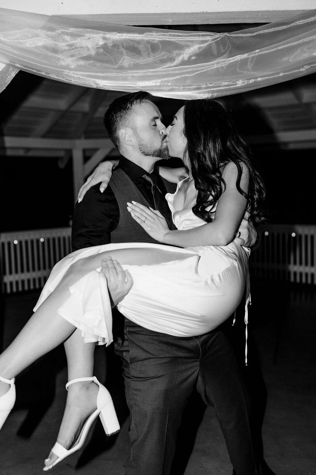 black and white photo of a groom holding a bride up as they kiss
