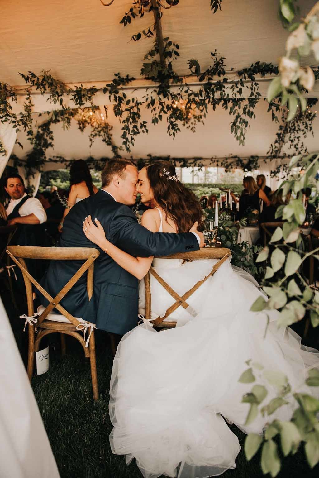 bride and groom kissing in their wedding reception tent covered in greenery