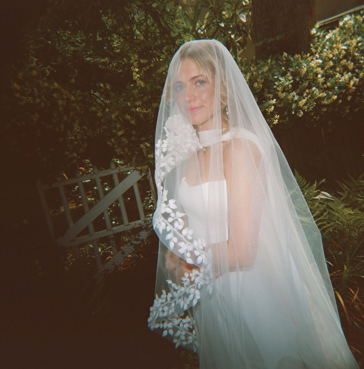Romantic editorial photo of a Charleston bride in a garden wearing a floral-trimmed veil.