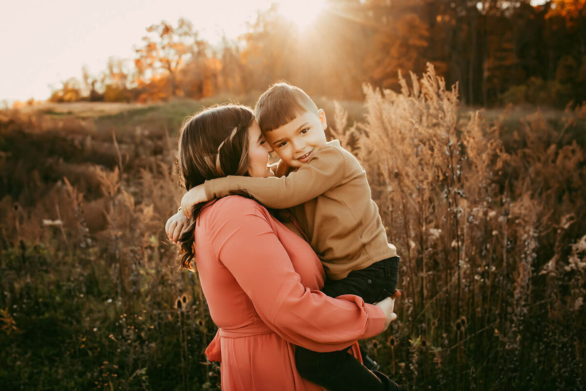 a mother holding her little boy with her nose to his cheek during golden hour