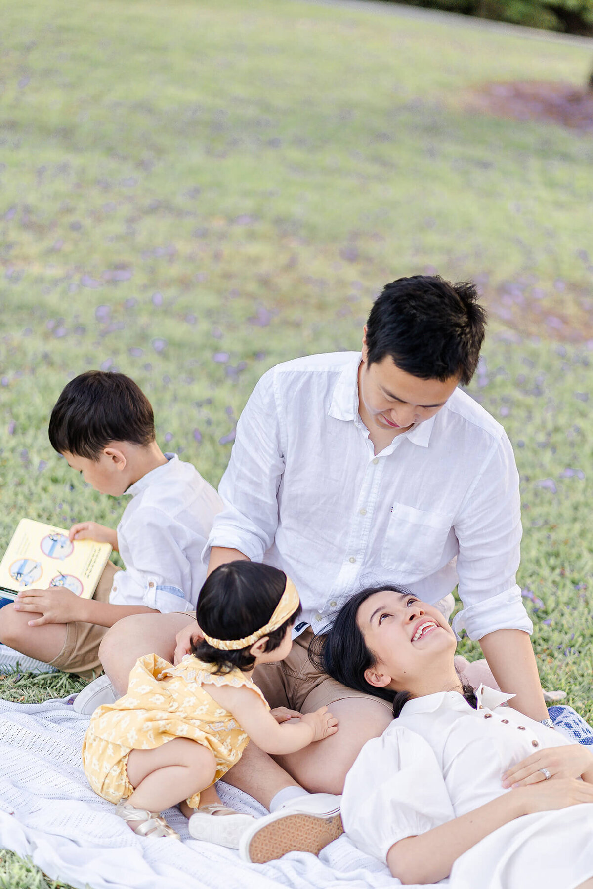 mum lying on dads laps and dad reading book to toddlers during family session in Brisbane
