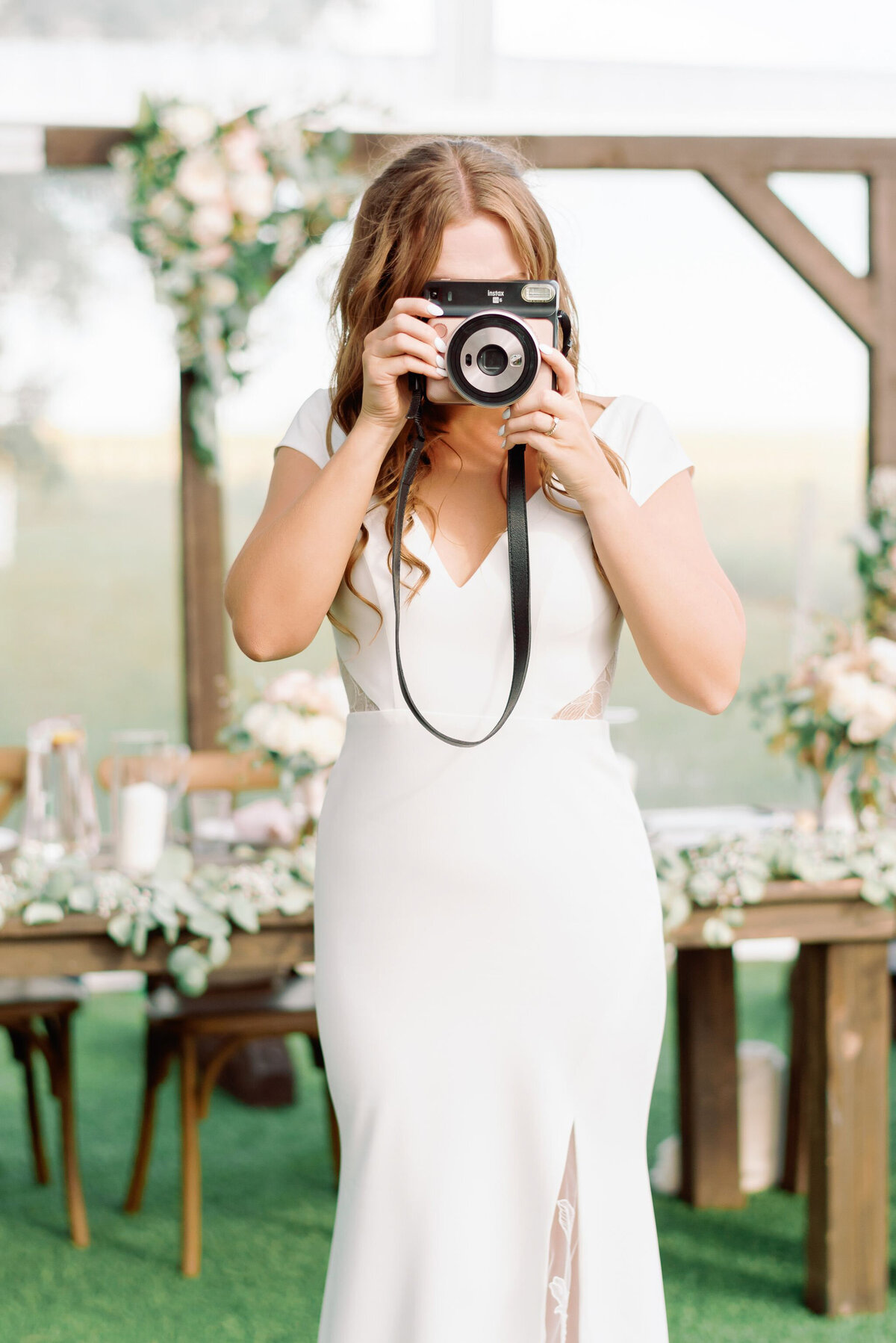 Fun bride taking photo with Polaroid camera, captured by Kaity Body Photography, elegant film inspired wedding photographer in Calgary, Alberta. Featured on the Bronte Bride Vendor Guide