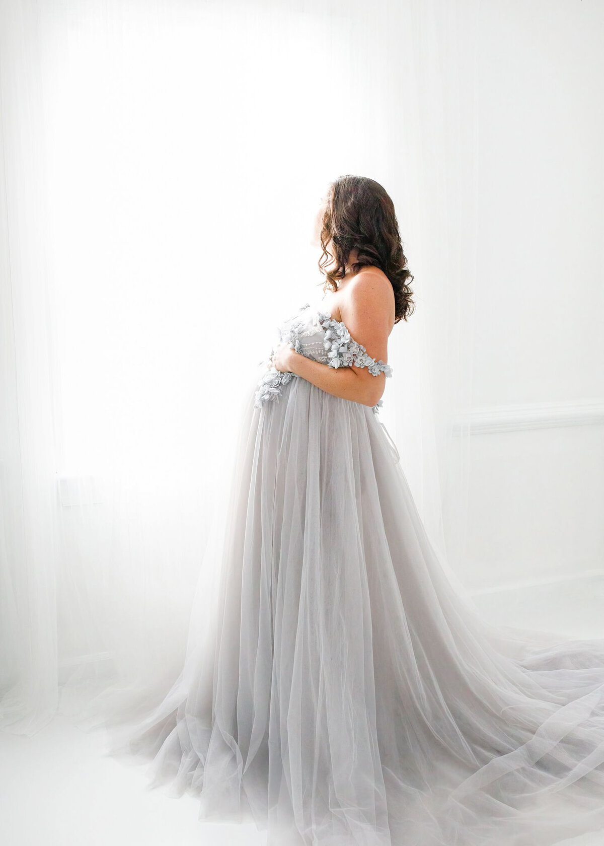 pregnant woman in a grey tulle gown looking out of the window