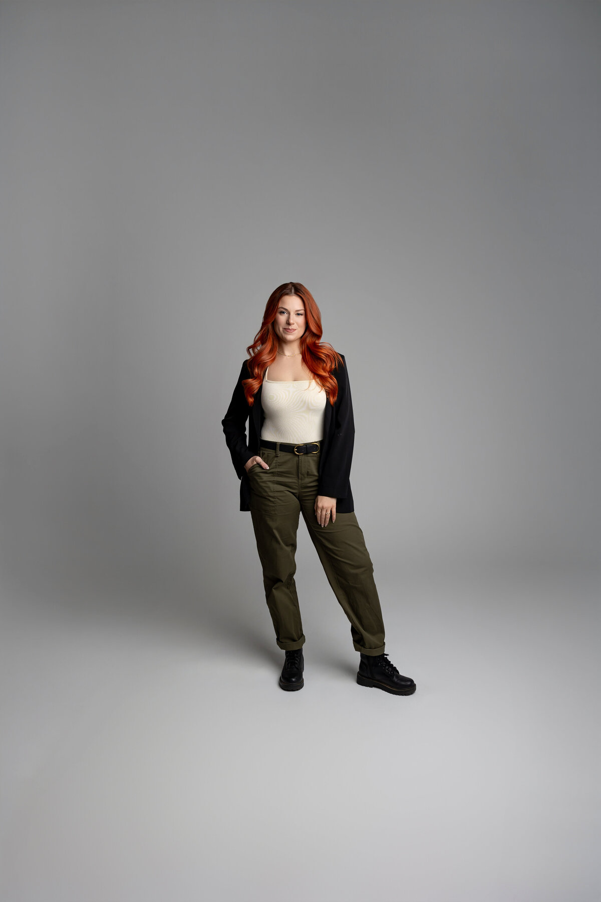 Woman with long red hair standing confidently with hand on hip in studio. Photograph by Yucaipa branding photographer Kaitlyn Dawn Photography.