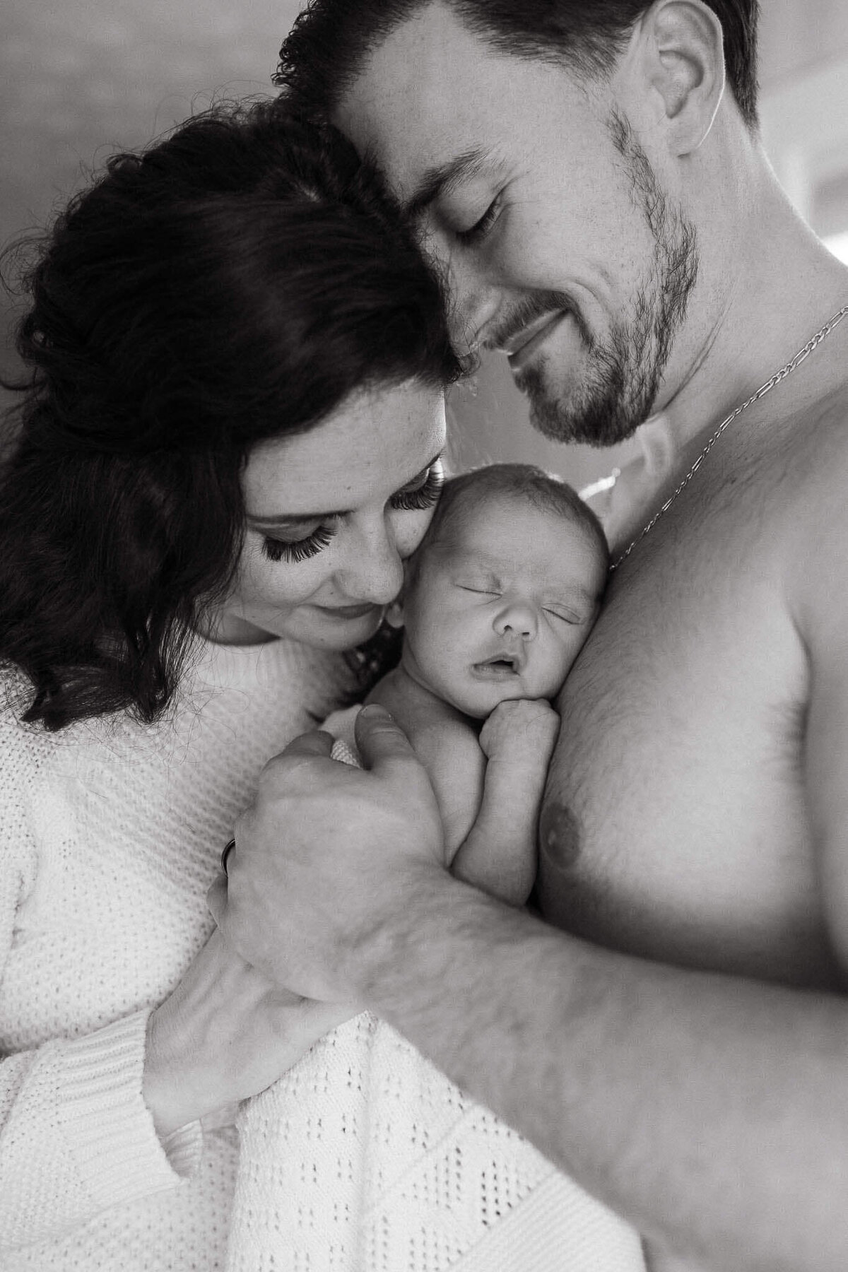 A heartfelt moment of parents cradling their newborn during a lifestyle photography session, captured in timeless black and white.
