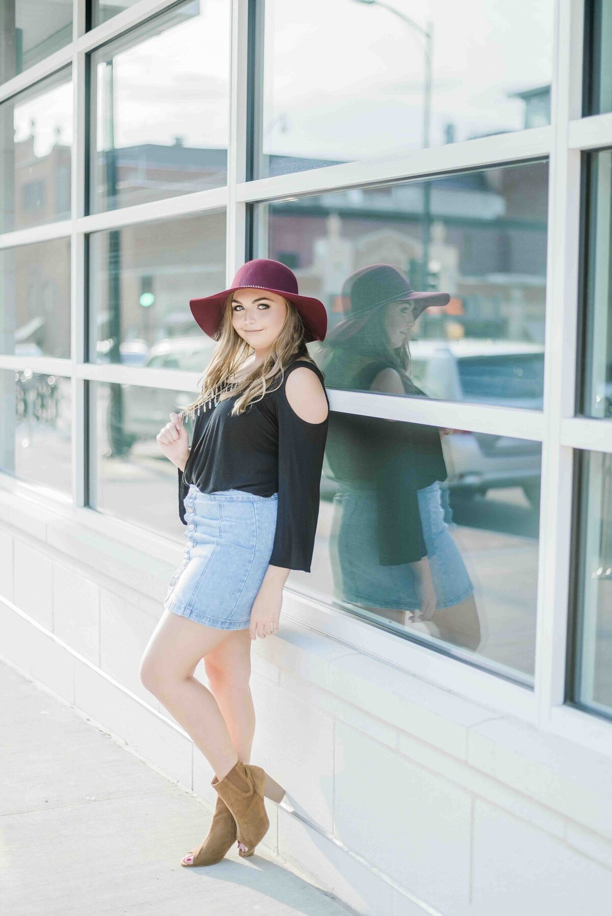 girl in a maroon sunhat leaning against a wall if reflective windows