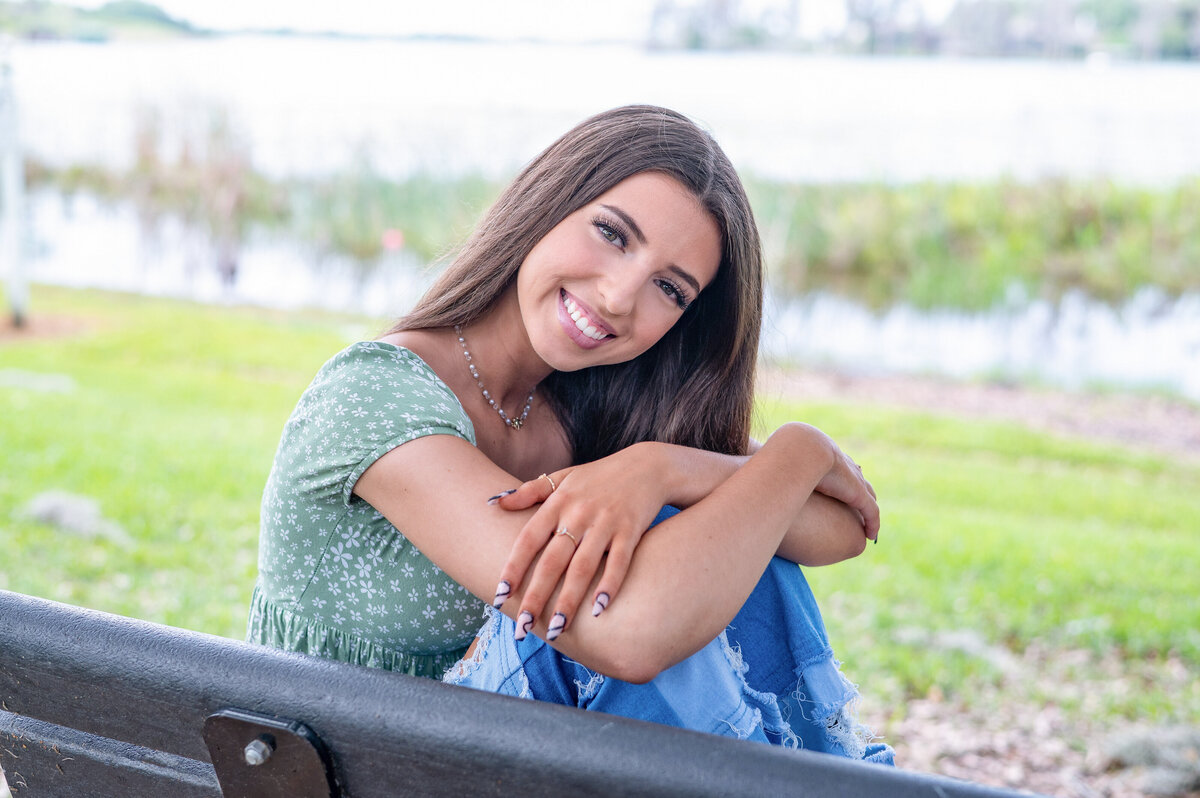 High school senior girl holding knees while smiling on a bench.