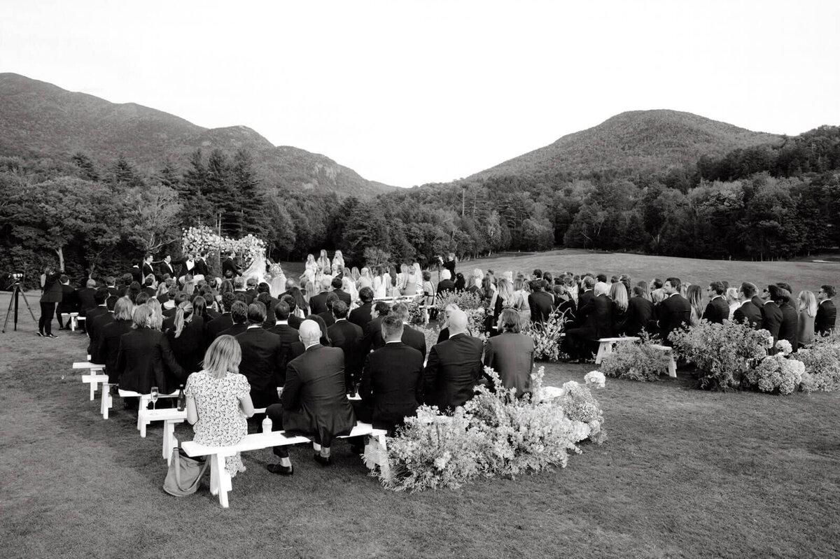 A beautiful wedding ceremony is being held at The Ausable Club, NY golf course, with magnificent mountains in the background.