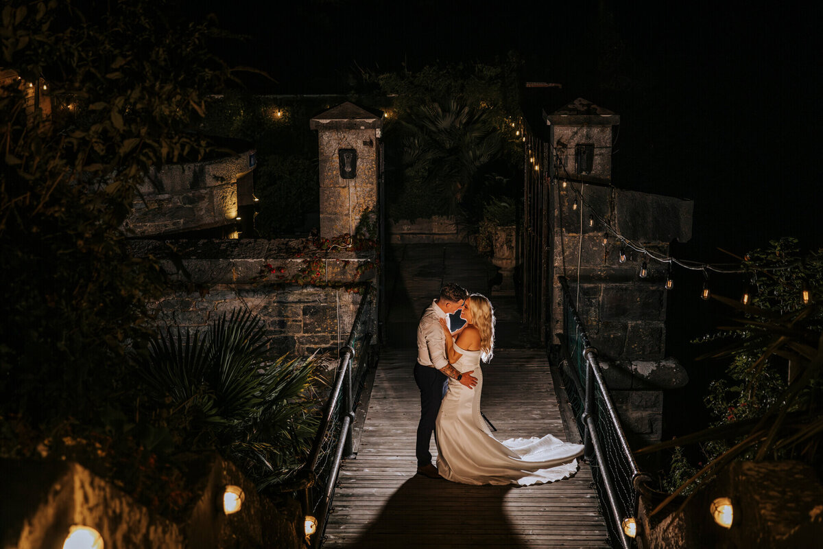 A bride and groom standing on a bridge at night