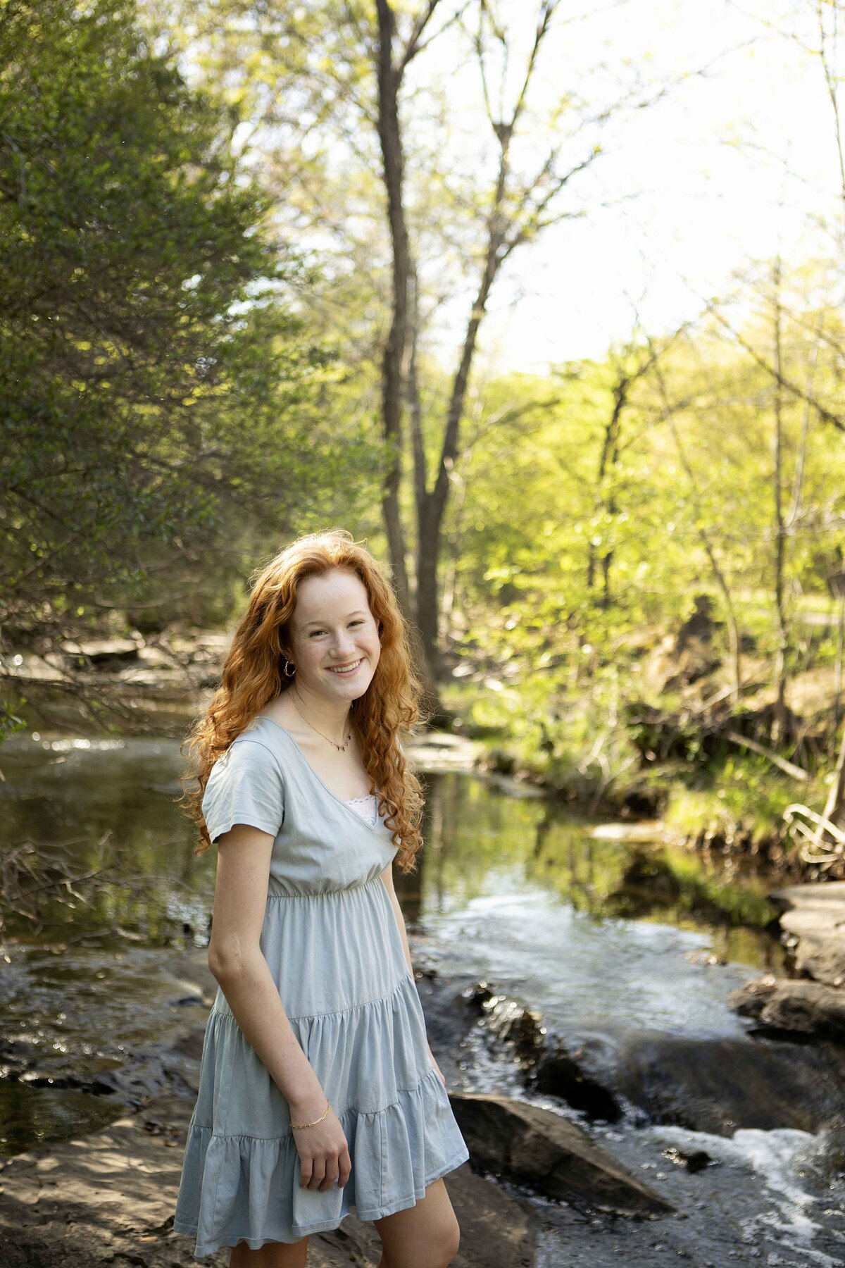 Middle sister playfully dipping her feet in the creek in Flower Mound, looking up and smiling during her solo photo session