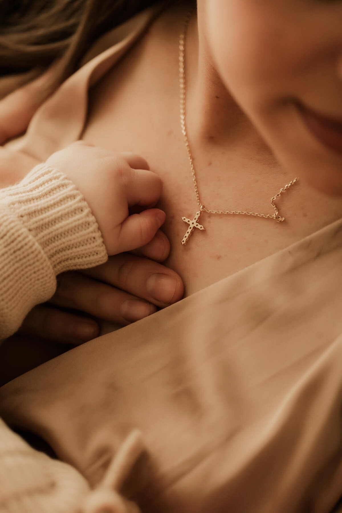 Baby girl's hand placed on her mothers next to the mother's cross necklace.