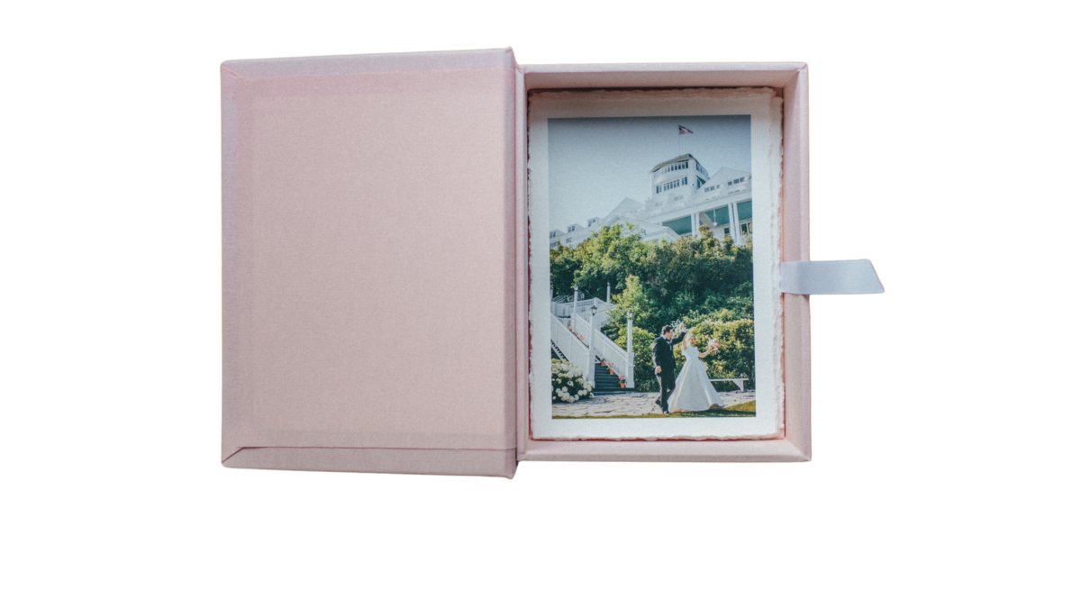 a pink print box for wedding couples with deckled prints inside and a white ribbon